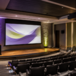 Modern presentation auditorium with large projection screen, ceiling-mounted projector, and tiered seating for Epson projection and Legrand Da-Lite screen solutions.