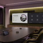 Modern hybrid meeting room with dual displays, video conferencing camera, microphones, and AV control panel for better collaboration.